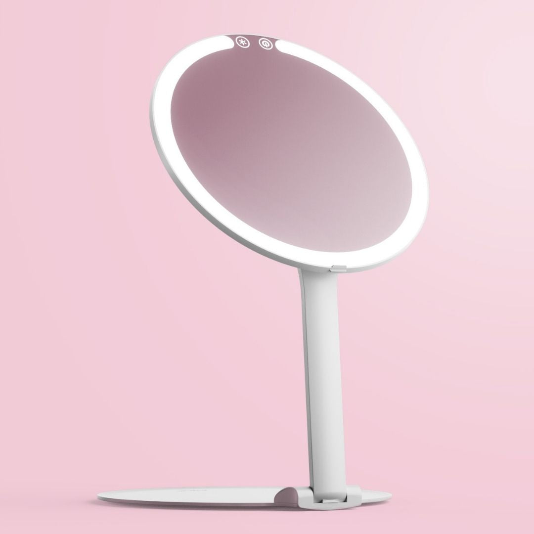 White Abigail LED travel makeup mirror with ring light and adjustable stand on a pink background.