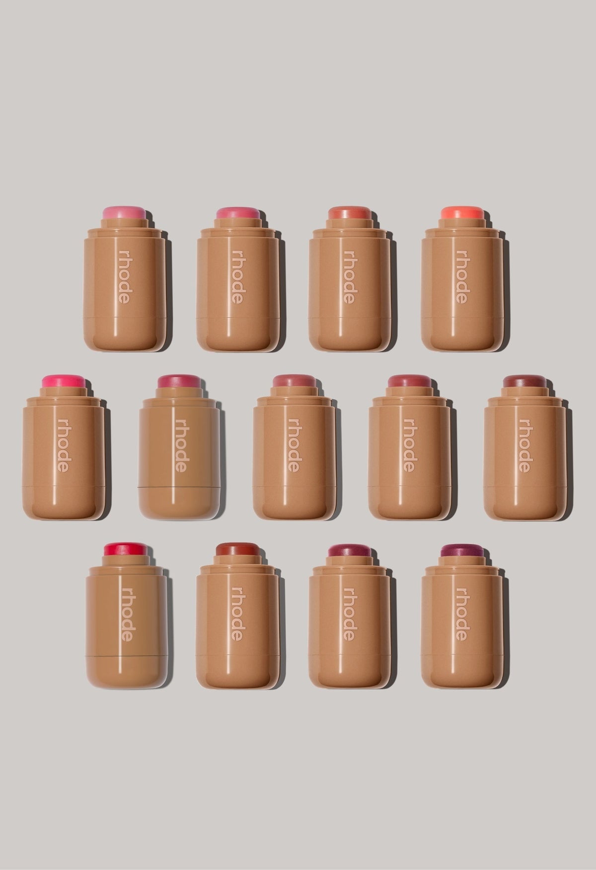 A collection of Rhode Pocket Blush cream makeup sticks in 13 dewy shades ranging from soft pinks to deep berry tones.
